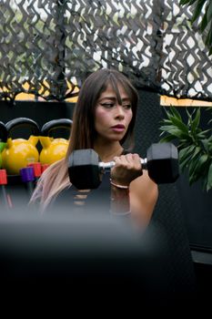A woman concentrating while lifting a dumbbell in an indoor gym setting surrounded by equipment.