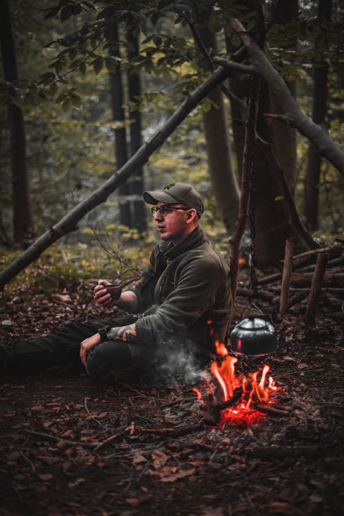 Free Traveler enjoying a peaceful break by a campfire in a dense forest, perfect for camping enthusiasts. Stock Photo