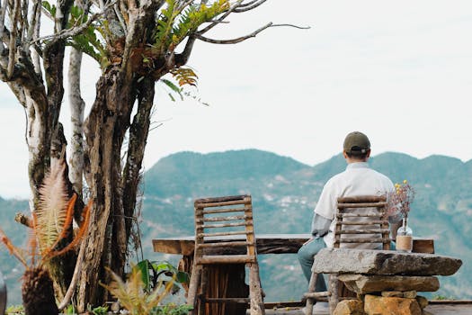Man sits on outdoor wooden furniture, enjoying a serene mountain vista.