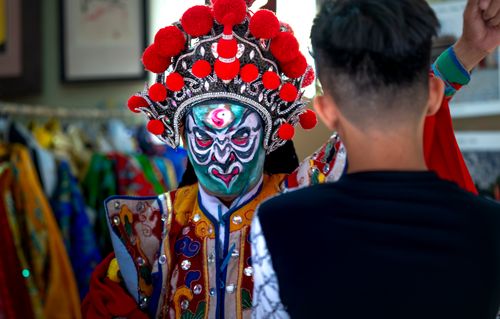 Free Colorful Chinese opera performer in intricate costume and face paint, adjusting attire backstage. Stock Photo
