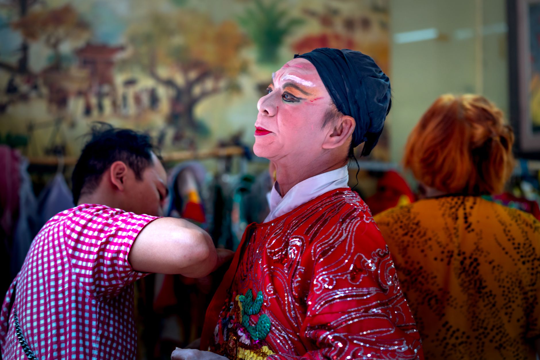 A performer preparing backstage in traditional Chinese opera costume and makeup.