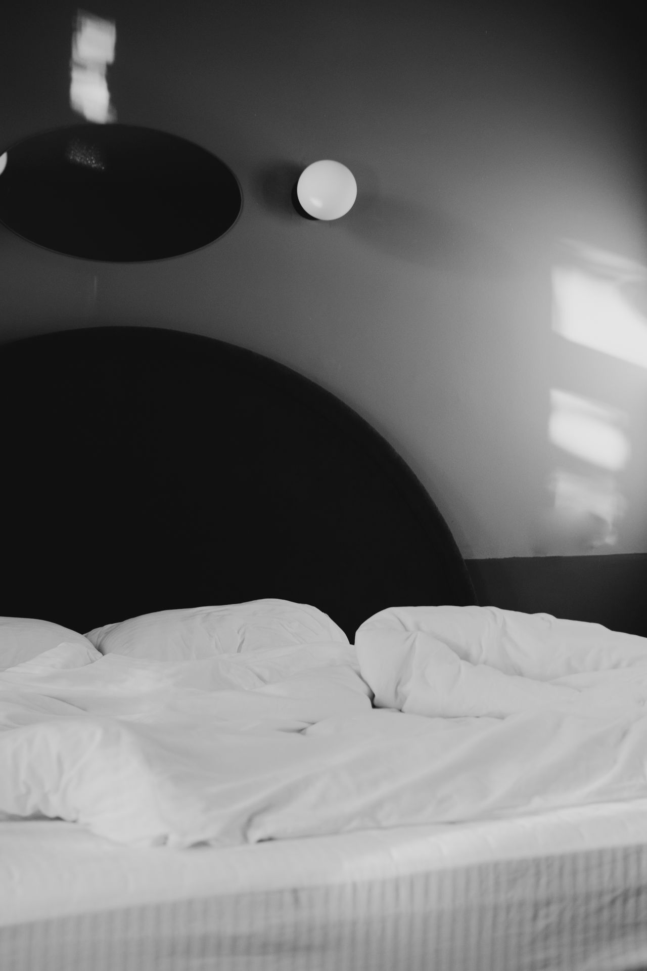 Moody black bedroom with an arched headboard, round mirror, and globe sconce