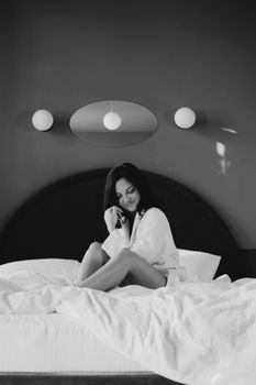 Monochrome photo of a smiling woman sitting on a bed in a cozy bedroom setting.