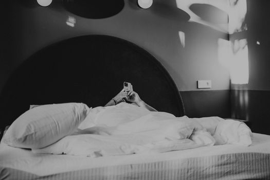 Monochromatic image of a person relaxing with a phone in a modern hotel room.
