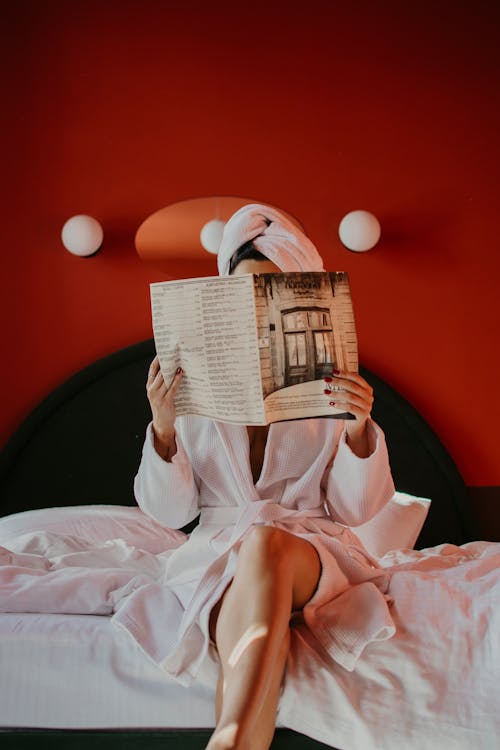 A Woman Sitting on a Bed Reading a Magazine