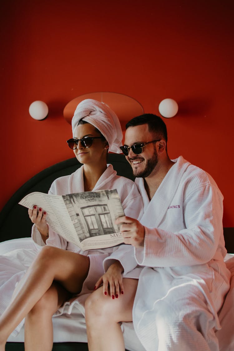 A Couple In Robes Reading A Magazine