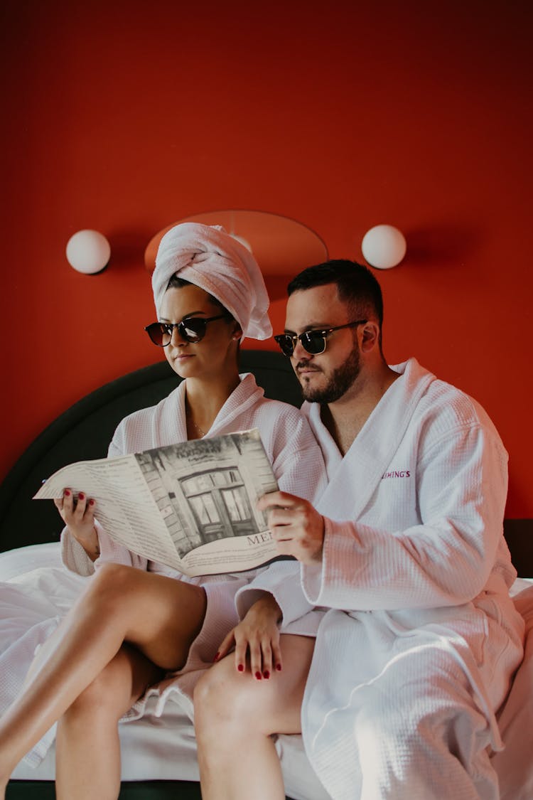 A Couple In Bathrobes Wearing Sunglasses Reading