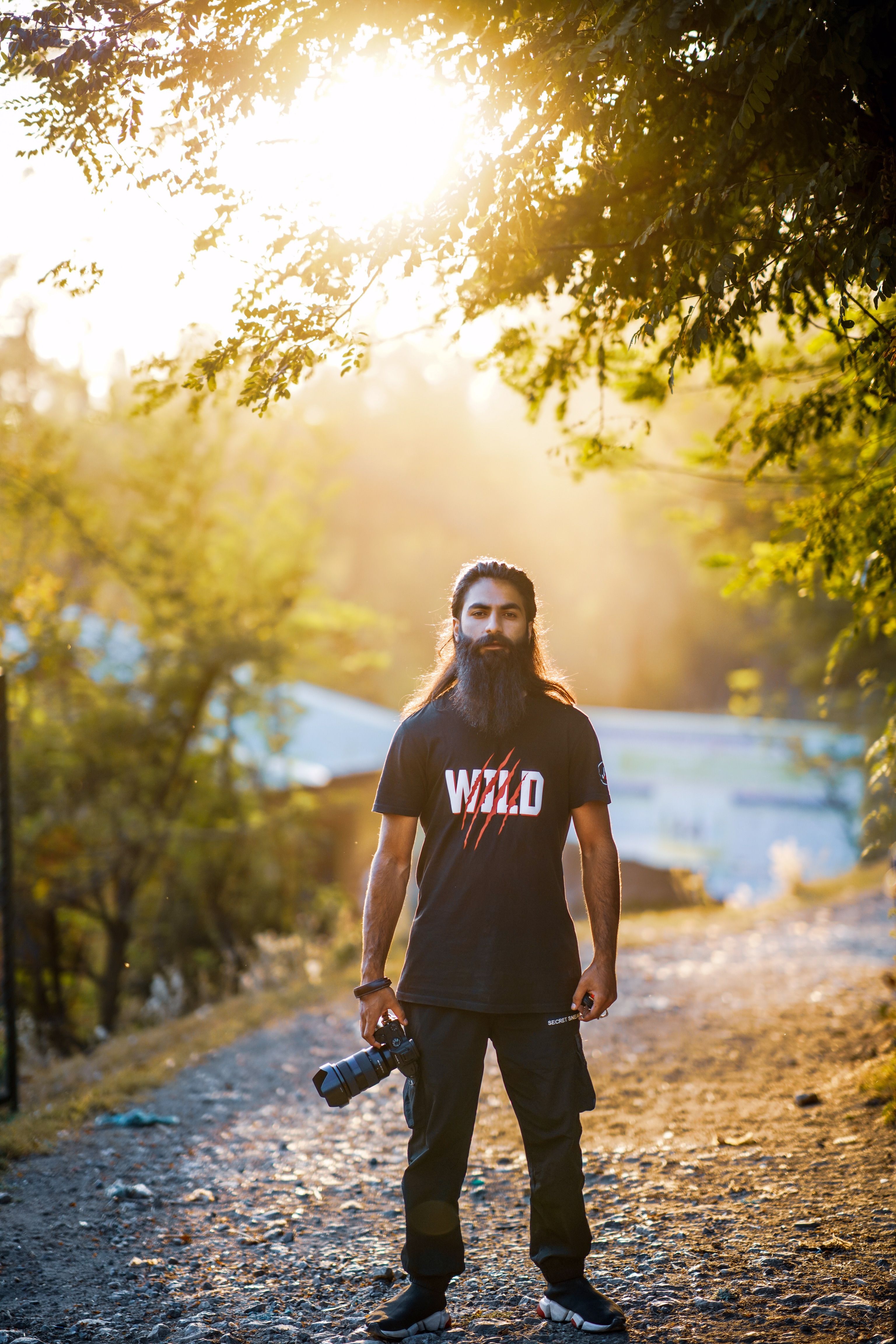 Portrait of a bearded man holding a camera on a sunlit path in Srinagar.