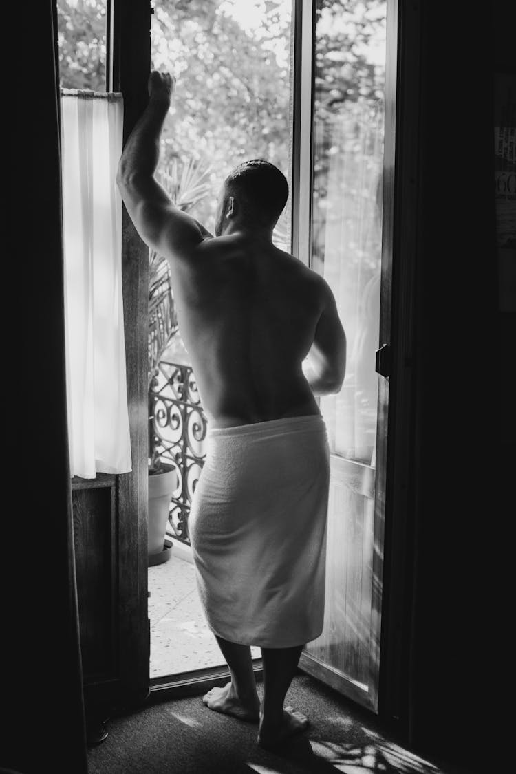 A Grayscale Photo Of A Shirtless Man Standing Near The Door