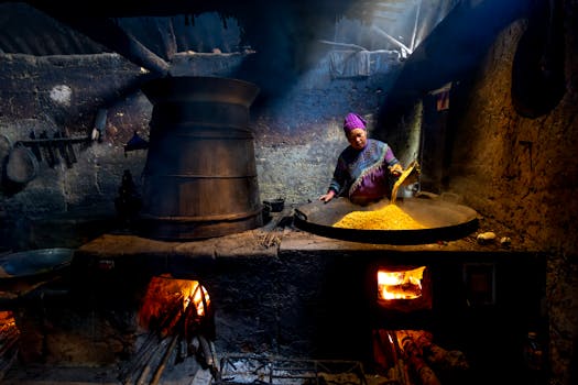 Woman cooking with traditional methods in rural setting, using a large cauldron over open fire.