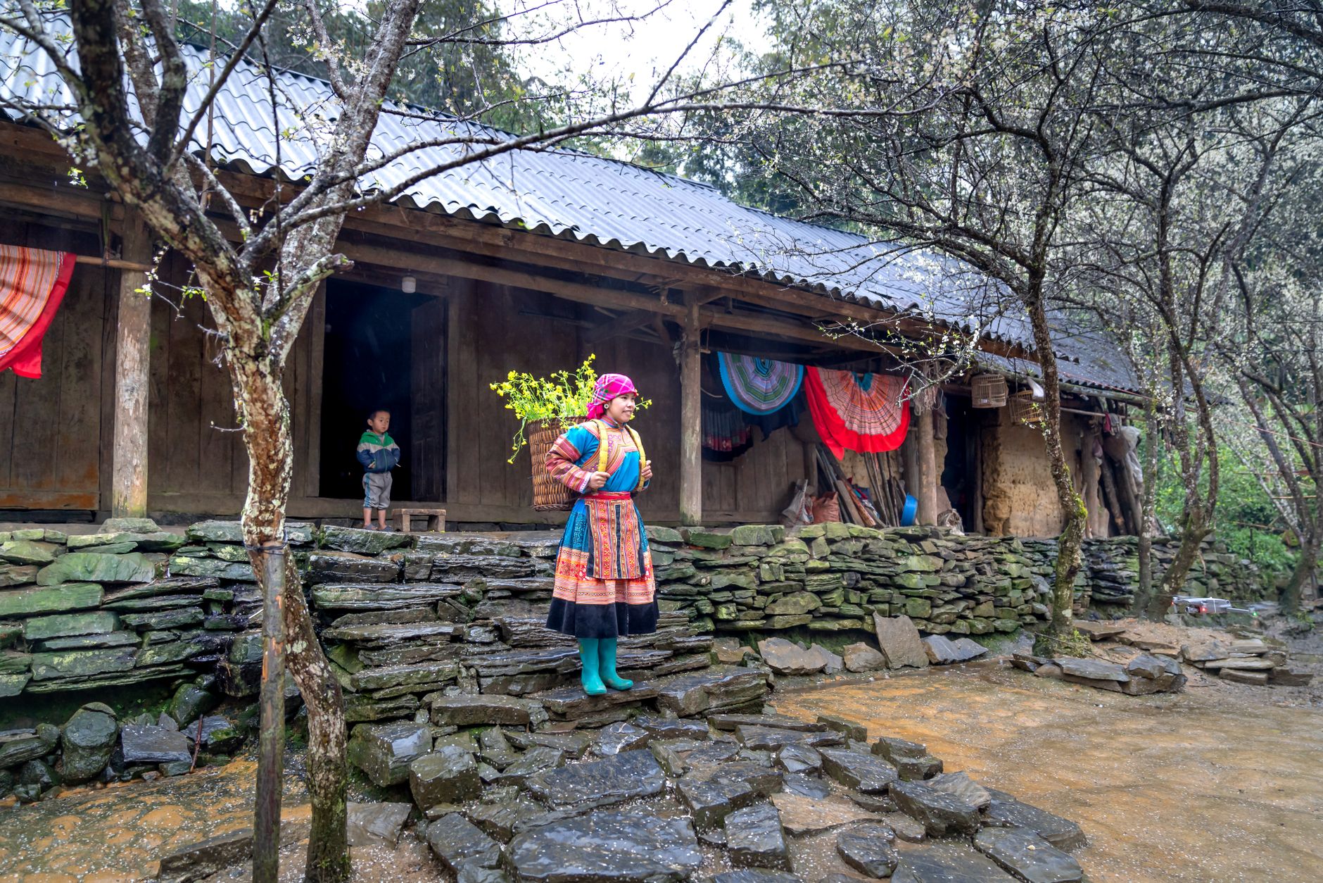 Woman and child in traditional attire at a rural village house with vibrant textiles.