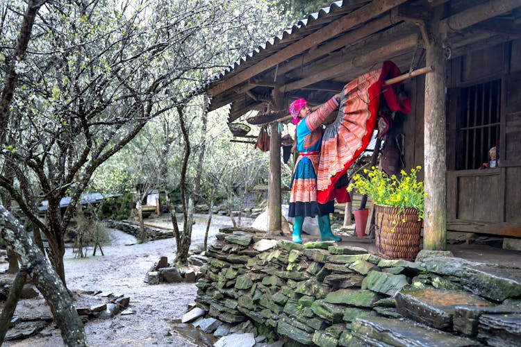 Woman In Traditional Clothes Hanging Skirt Near House