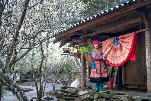 Free Woman in vibrant traditional clothing outside a wooden hut in a spring village setting. Stock Photo