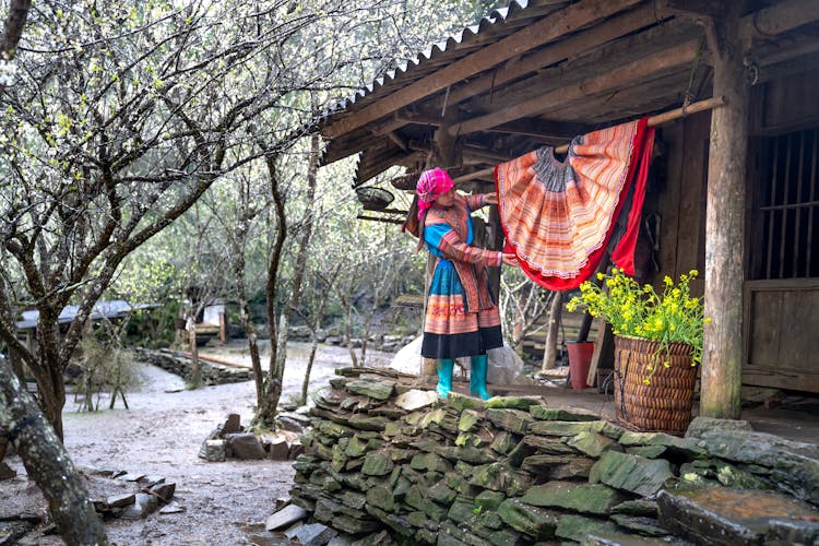 Woman In Traditional Costume Hanging Clothes Near House