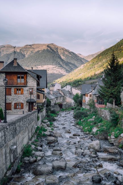 Picturesque view of Vielha village with mountain backdrop and flowing river.