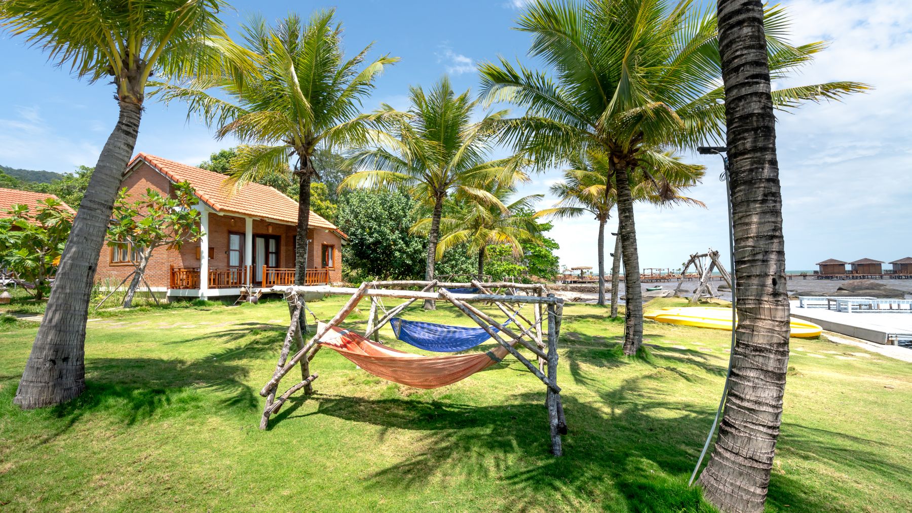 A serene view of bungalows and hammocks under palm trees by the beach.