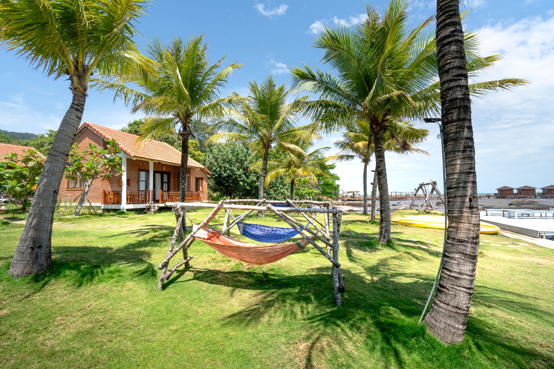 A serene view of bungalows and hammocks under palm trees by the beach.