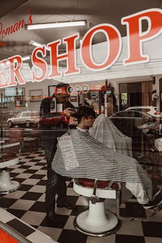 A barber is giving a haircut inside a classic barbershop, captured through the window.