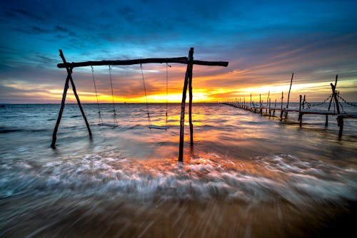 Scenic View of a Wooden Footbridge and Swing on Sea During Golden Hour