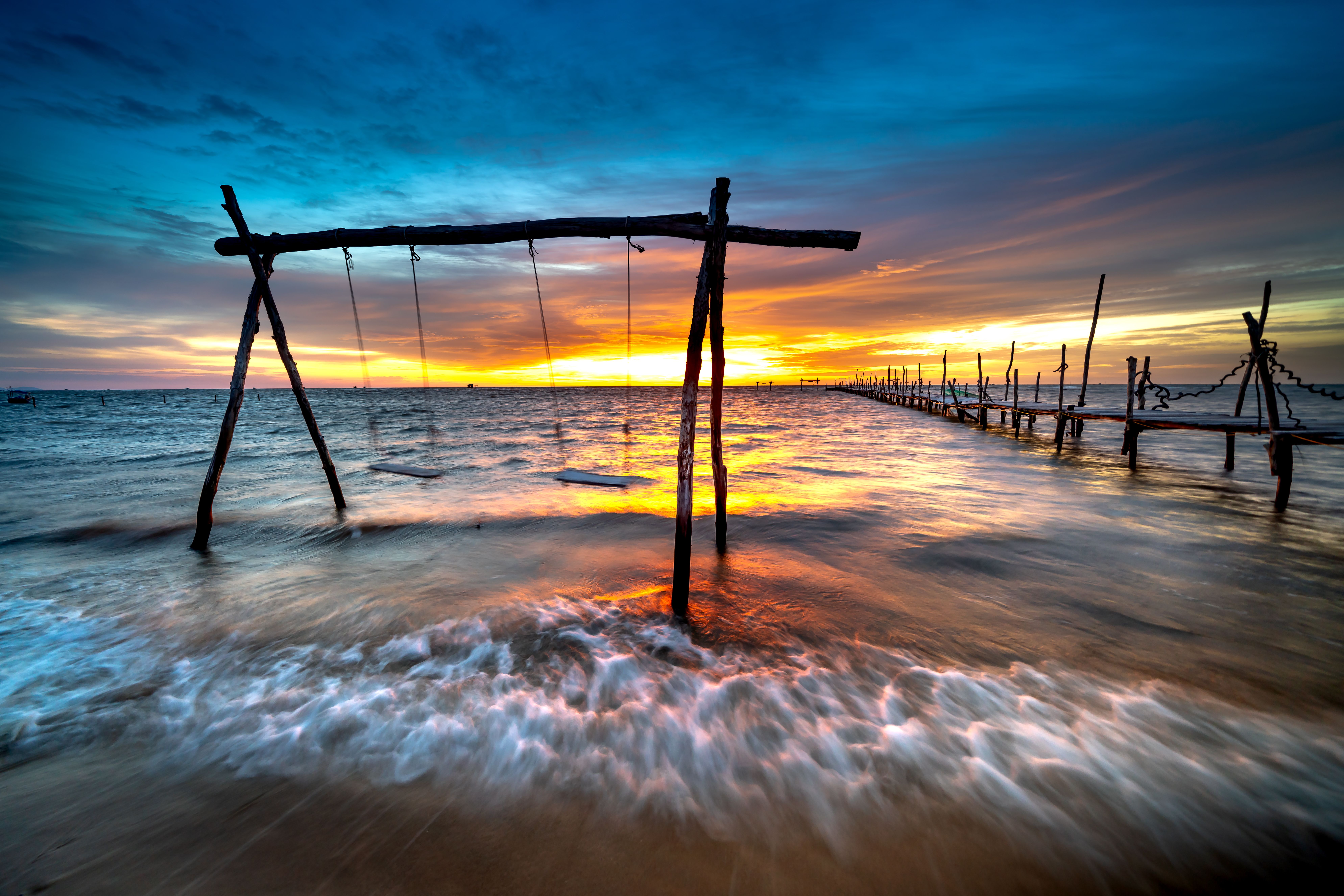 Wooden swing set over ocean waves during a vibrant sunset. Perfect for tranquil escapes.