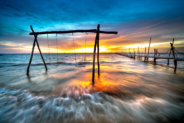 Swing And Pier On Beach At Sunset