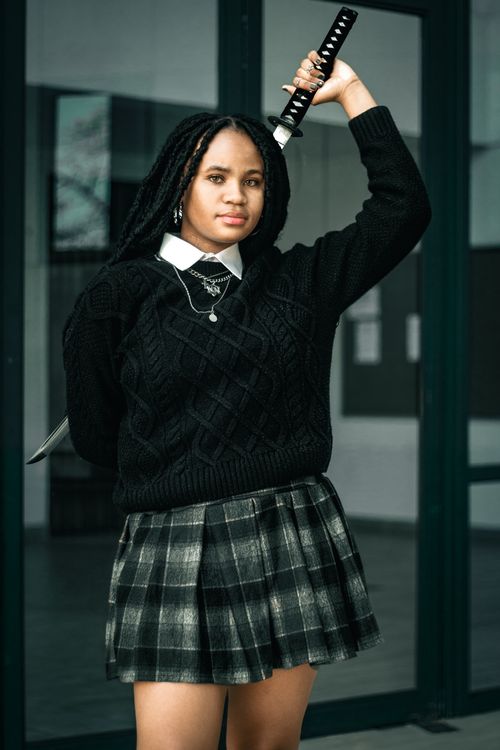 Free Stylish portrait of a woman posing with a sword, wearing a black sweater and plaid skirt indoors. Stock Photo