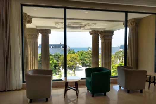 Chic interior with armchairs, facing picturesque ocean view through classic columns.