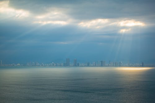 Modern City Skyline across the Water under a Cloudy Sky with Sun Rays 