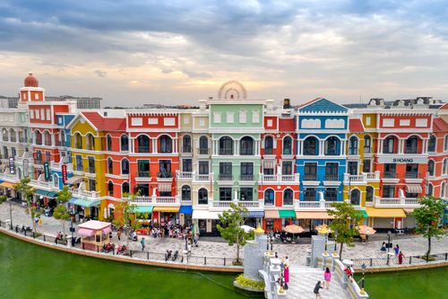 Free Vibrant resort scene at Grand World Phu Quoc with colorful facades and people walking by the water. Stock Photo