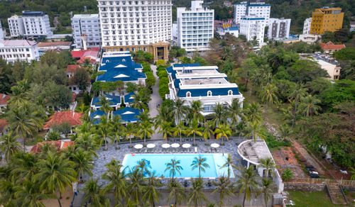 Free Aerial shot of a resort complex with swimming pool, surrounded by palm trees and city buildings. Stock Photo
