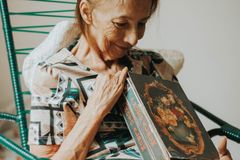 An elderly woman smiling warmly while holding a vintage photo album indoors.