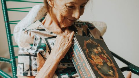 An elderly woman smiling warmly while holding a vintage photo album indoors.