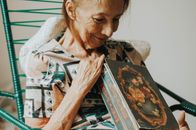 An elderly woman smiling warmly while holding a vintage photo album indoors.