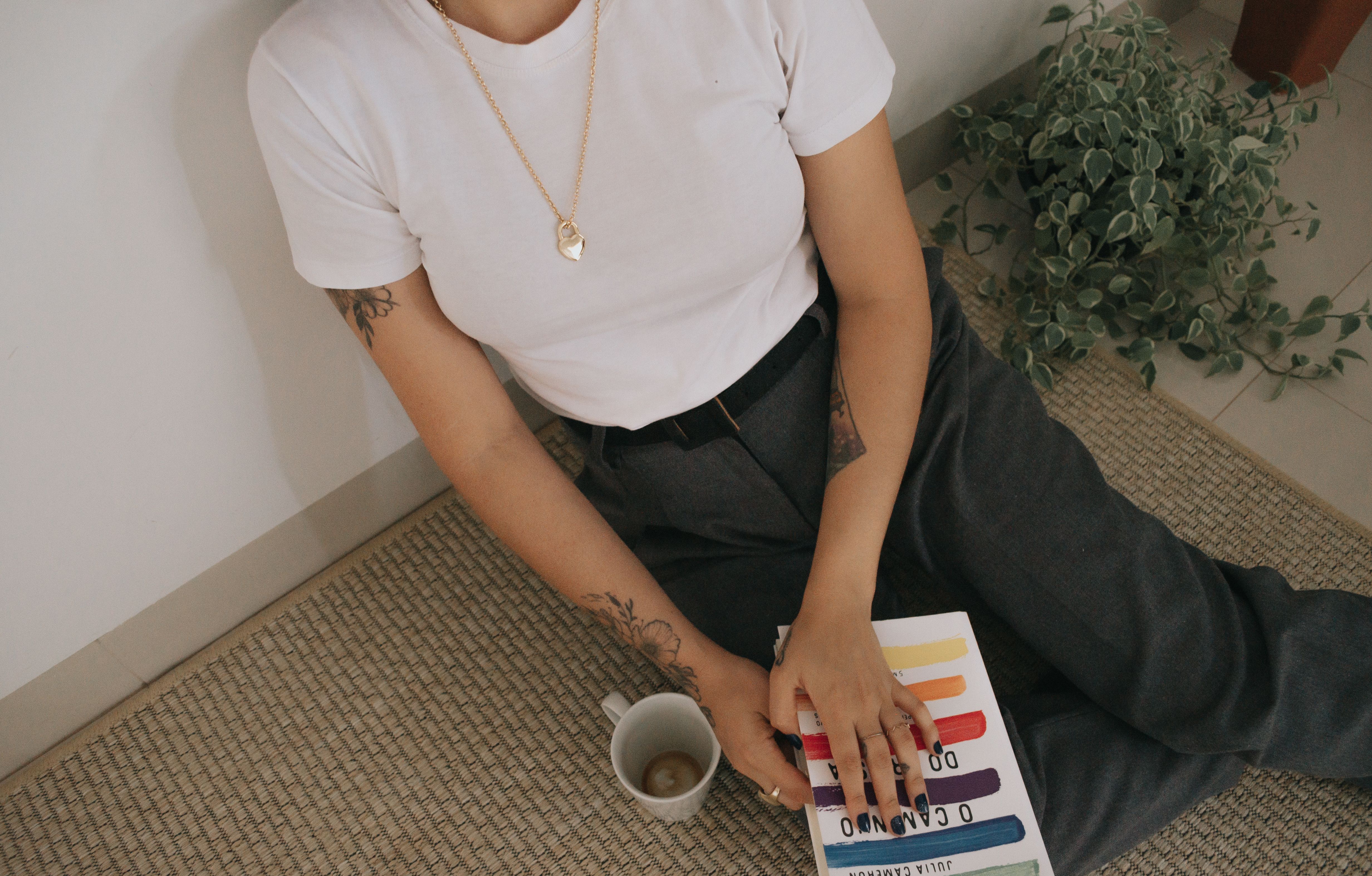 Woman sitting on rug, reading a colorful book with coffee cup nearby.