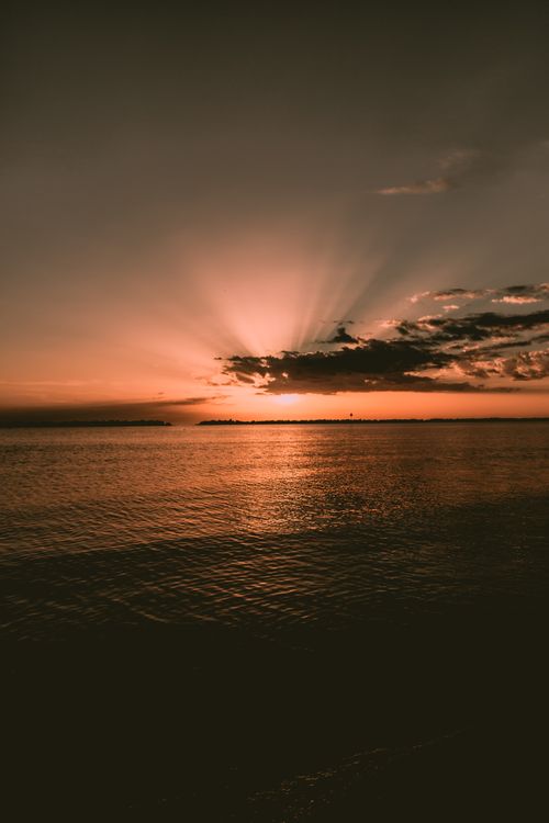 Free Captivating sunset over the ocean with dramatic clouds and warm afterglow. Stock Photo