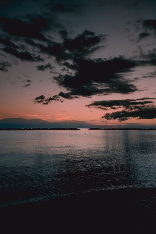Free Capture of a scenic sunset with dark clouds over a calm sea, perfect for mobile wallpaper. Stock Photo