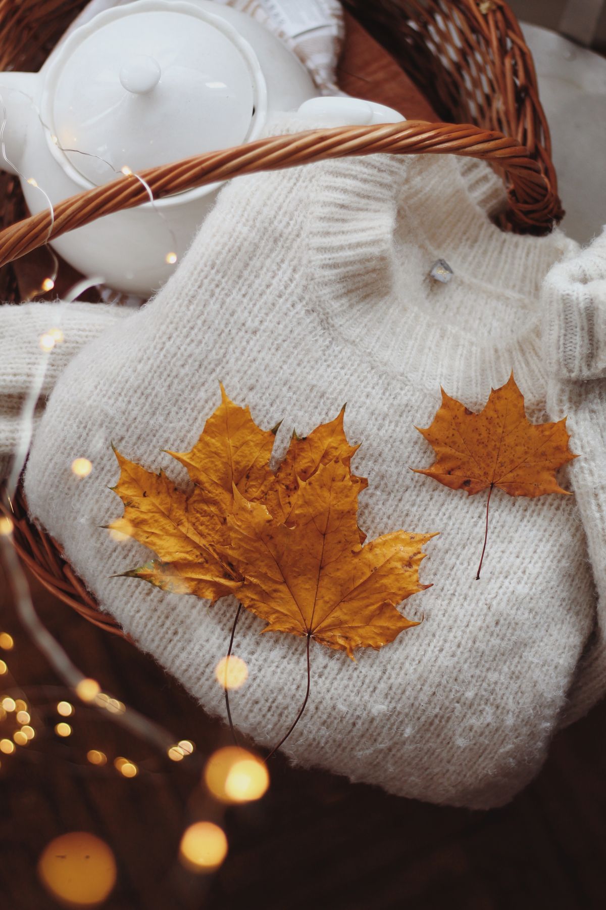 Warm fall scene with a knitted sweater, maple leaves, and a teapot in a basket.