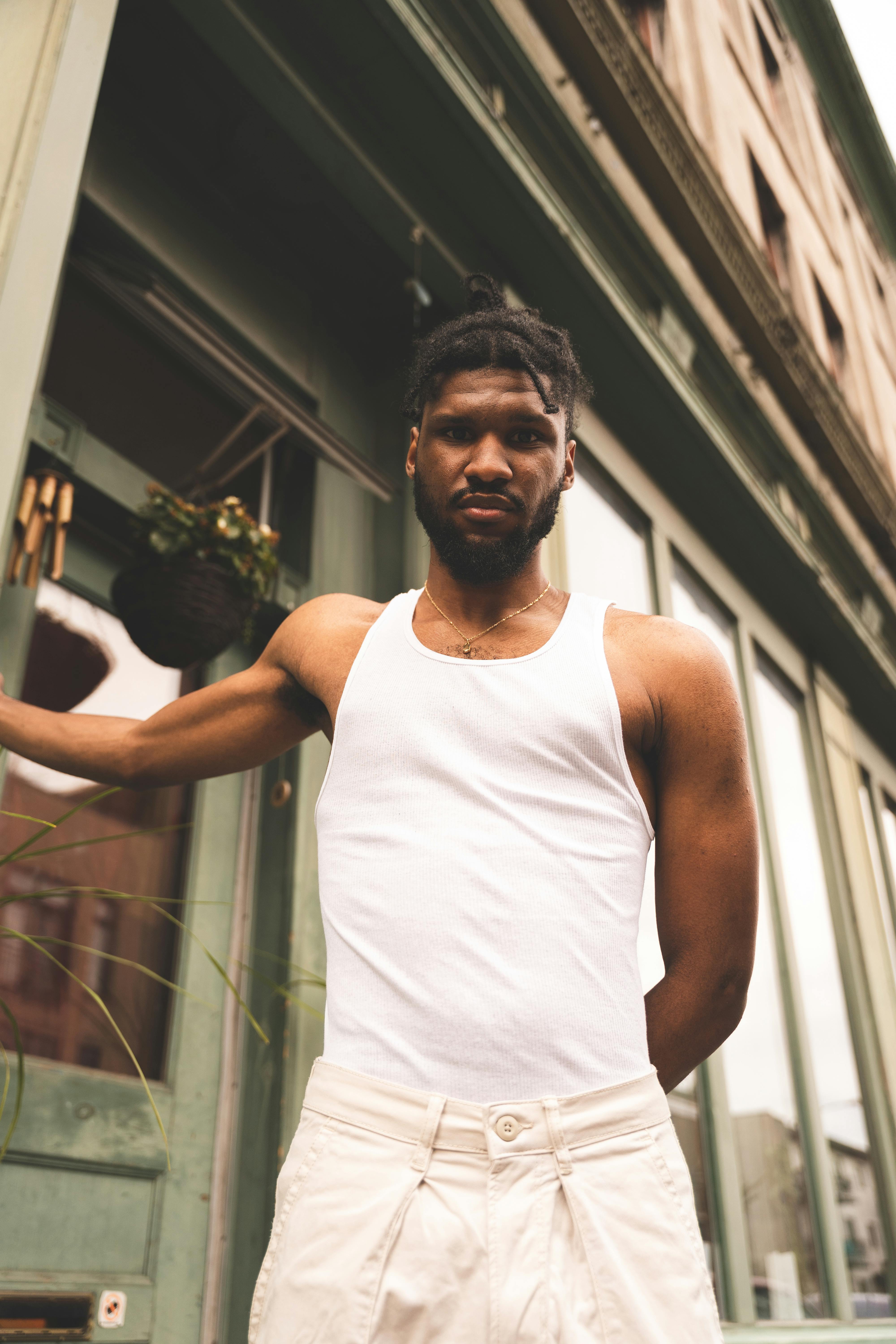 Portrait of a man in a white tank top standing outdoors in Montréal, exuding confidence.