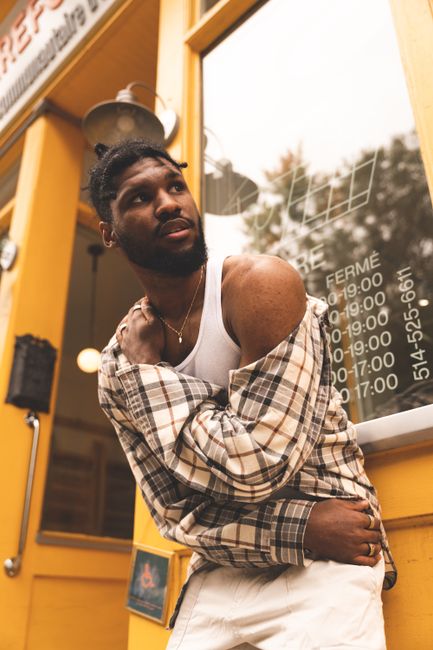 Fashionable man in plaid shirt and tank top posing outside a storefront.