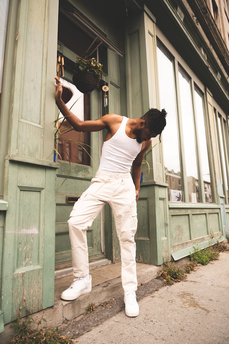 A Man In White Tank Top  Standing On The Street While Looking Down