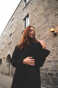 Fashionable woman with brown hair posing against a historic stone building in Montreal.