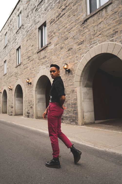 Free Stylish young man in pink pants walks past stone arches in Montréal. Stock Photo