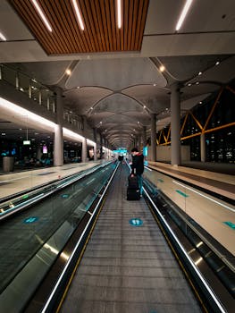 A traveler moves along a moving walkway inside a modern airport terminal.
