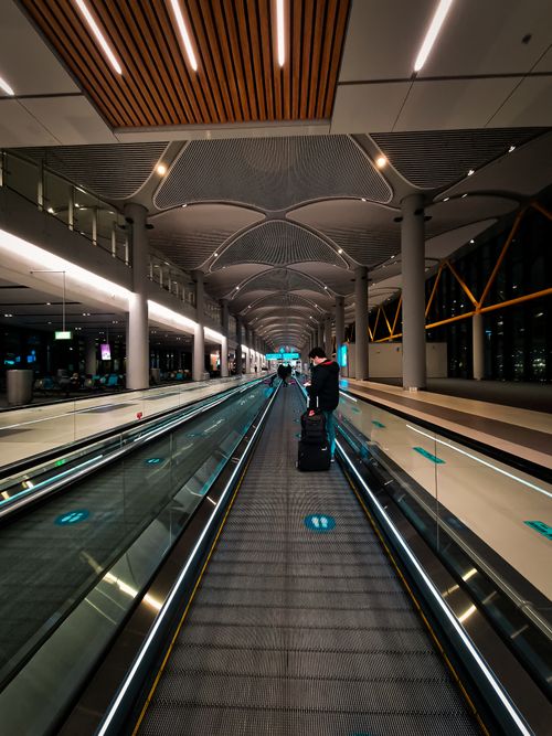Free A traveler moves along a moving walkway inside a modern airport terminal. Stock Photo