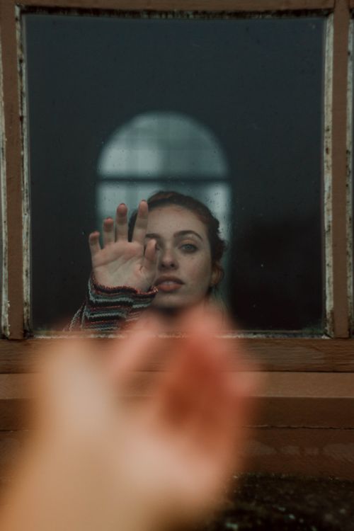 Free Woman reaching out through a glass window, conveying longing or sadness. Stock Photo