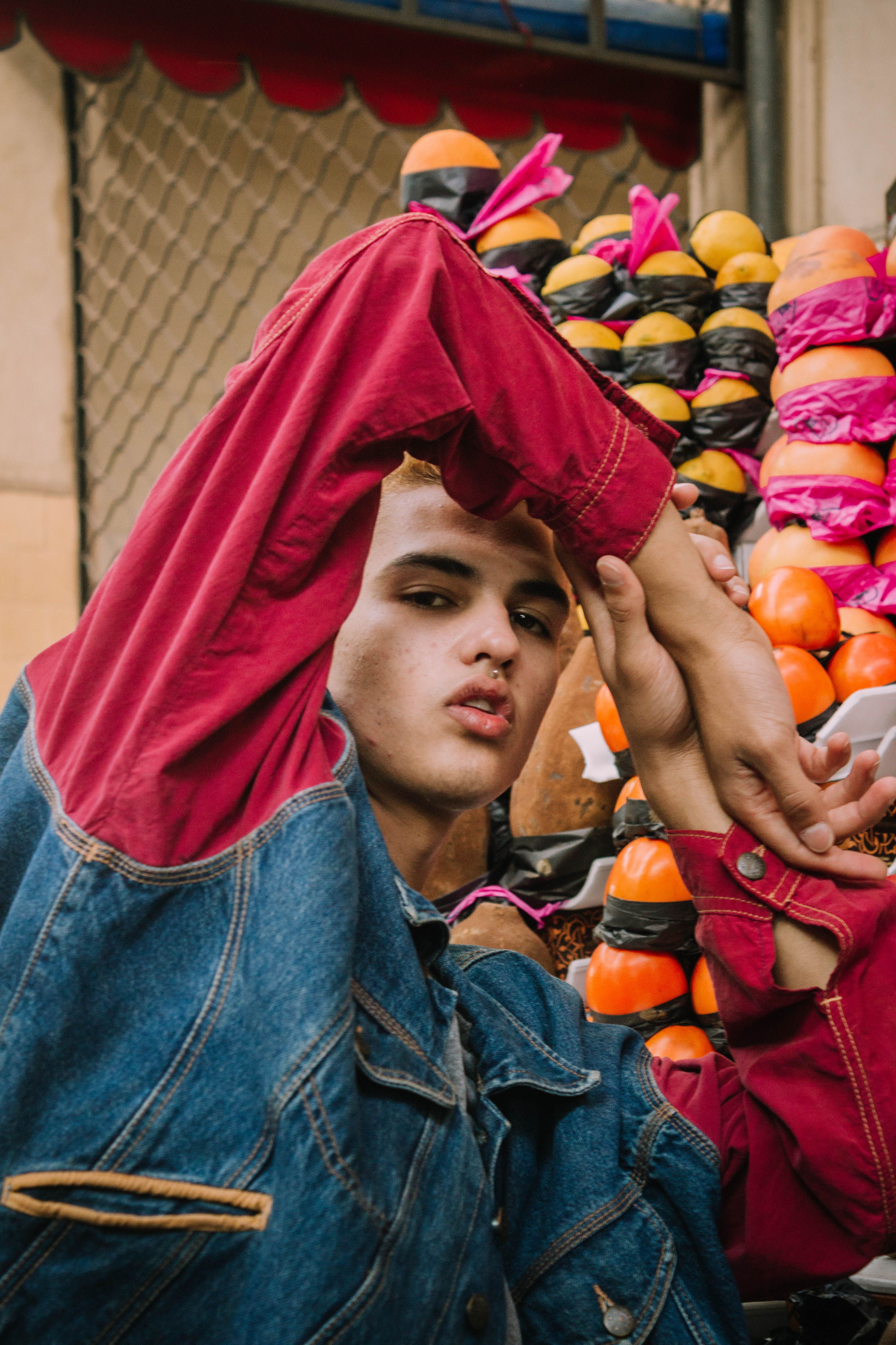 Young man posing fashionably in denim against a colorful backdrop of artfully stacked objects.