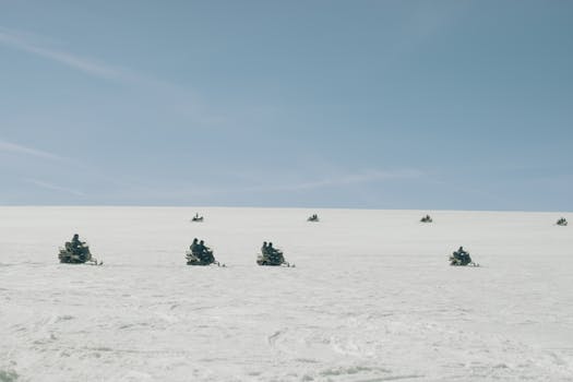 A group of people on snowmobiles exploring a snowy field under a clear blue sky.