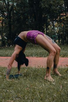 Tattooed woman doing a backbend yoga pose on grass, showcasing flexibility and fitness.