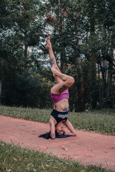 Fit woman performs a headstand yoga pose in a serene public park setting.