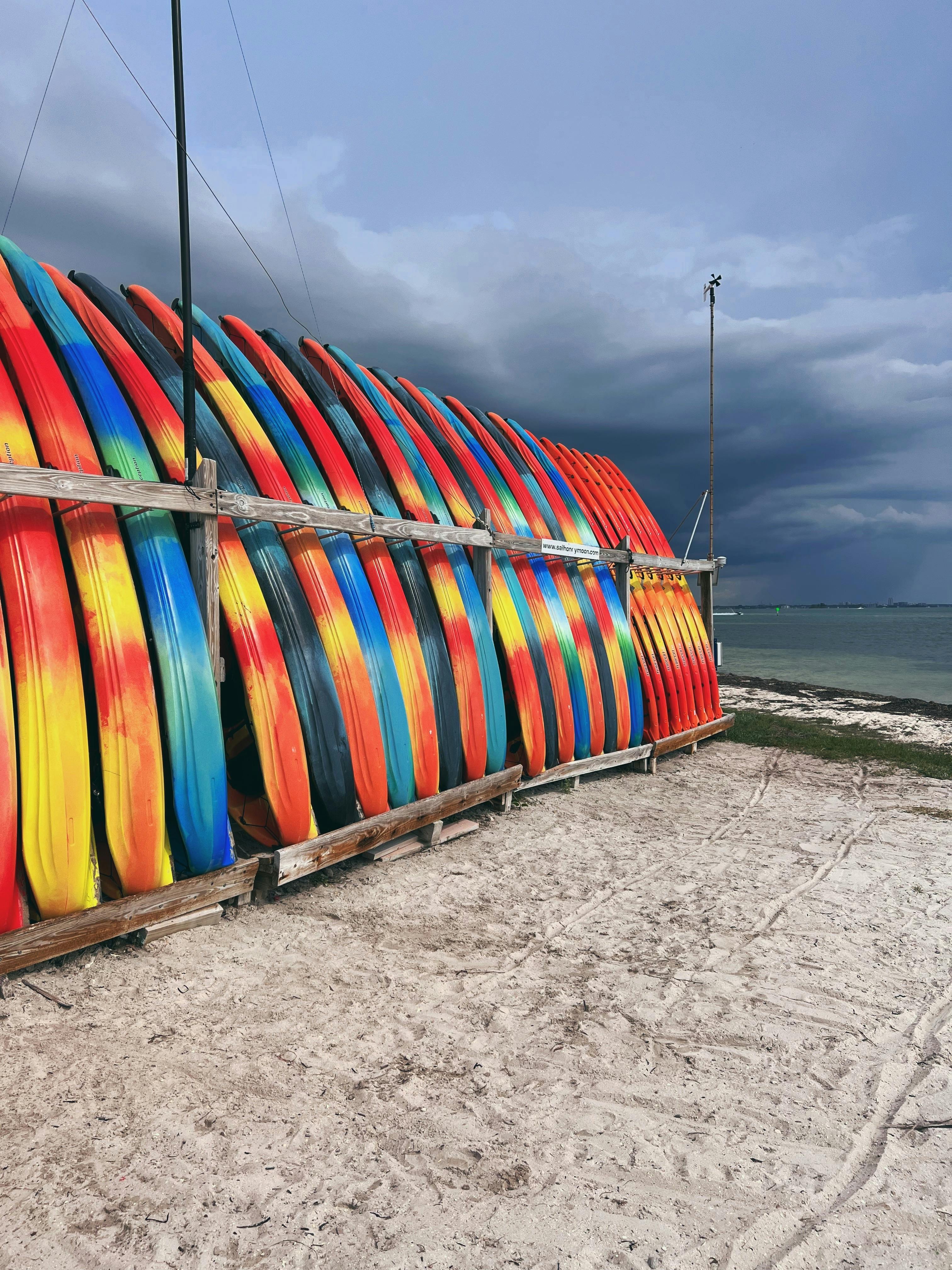 Vibrant kayaks stacked on sandy Clearwater Beach with dramatic clouds overhead.